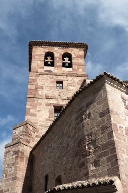 Uzun taş kule, kavisli pencereler, eski bir binanın parçası, bulutlu bir gökyüzünün arka planına karşı.