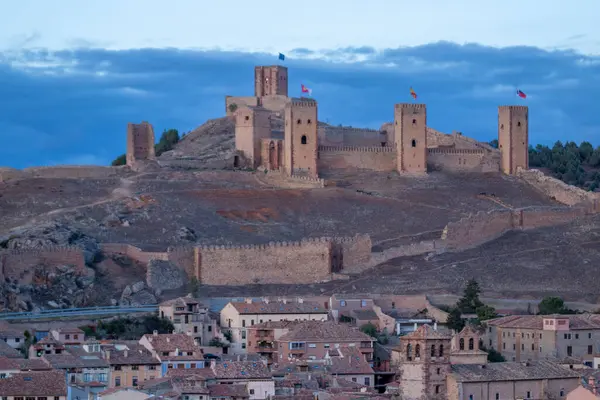 stock image stone castle overlooks a quaint town, flags waving, under a soft evening sky, blending history and natural beauty