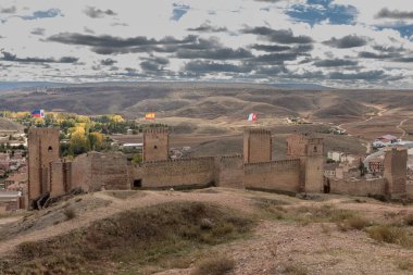 Kulelerin tepesinde bayrakları olan antik taş kale parlak, bulutlu bir gökyüzünün altındaki vadiye bakıyor.