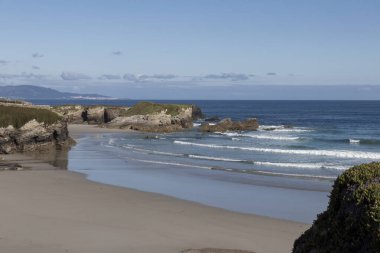 Kayalık oluşumları, yumuşak dalgaları, berrak gökyüzü ve uzak dağları ile sakin ve doğal güzelliği olan sakin bir sahil..