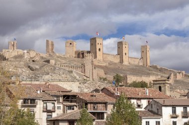 Taştan kale, aşağıdaki köy, kulelerde bayraklar, parçalı bulutlu gökyüzü, tarihi ortam, sabah ya da akşam ışığı