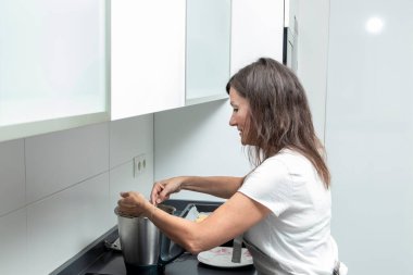 Mutfakta, tencereyi fırında karıştıran, yüzü kahverengi bir dikdörtgen ile gizlenmiş bir insan.