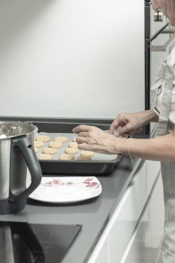 Kişi yemek tepsisine kurabiye yerleştiriyor. Bu da mutfak ortamında ev yapımı bir etkinlik olduğunu gösteriyor.