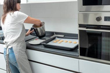 Kadın mutfakta kurabiye pişiriyor. Kontun üzerine bir tavaya bir karışım döküyor.