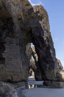 Kumlu bir plajda mavi gökyüzü arka planına sahip doğal kaya kemeri oluşumları. Kıyı jeolojik yapısına bakış