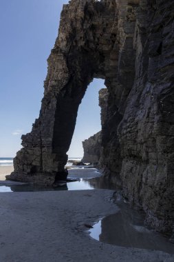 Sahilde gökyüzünü yansıtan bir Rocky kemeri. Doğal kaya oluşumu ve kıyı manzarası konsepti