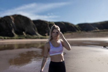 Güneşli bir plajda arka planda dağlarla dikilmiş, yüzündeki kılları fırçalıyordu.