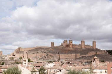Bulutlu bir gökyüzünün altındaki kuleleri ve köyü çevreleyen ortaçağ tepe kalesinin panoramik manzarası..