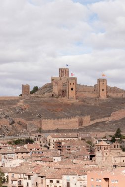 Bulutlu bir gökyüzünün altında geleneksel bir İspanyol köyüne bakan bir tepenin üzerindeki tarihi şato.
