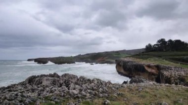Güçlü okyanus dalgalarının bulutlu gökyüzünün altındaki kayalıklara çarptığı Asturias 'ın engebeli kıyı şeridinin çarpıcı manzarası.