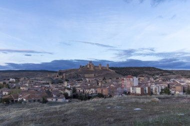 Evening View of a Spanish Town with Historic Castle on Hill Under a Cloudy Sky clipart