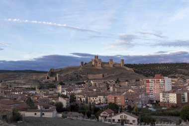 Panoramic view of a historic hilltop castle overlooking a mix of traditional and modern buildings at sunset. clipart