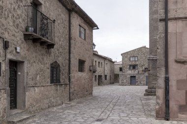 Quiet cobblestone street in a historic European village surrounded by rustic stone buildings and iron balconies. clipart