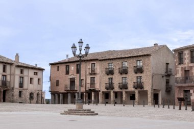 Historic town square with traditional stone buildings and a central lamppost under a cloudy sky. clipart