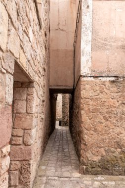 Narrow stone alleyway in a historic village with weathered walls and a cobblestone path. clipart