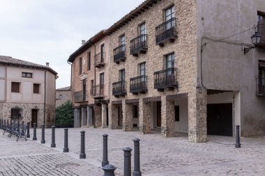 Taş binaları, demir balkonları ve kaldırım taşı plazası olan tarihi bir köy meydanı.