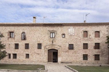 Karmaşık bir kapı aralığı, küçük pencereleri ve küçük bir arması olan tarihi taş bina. Parçalı bulutlu bir gökyüzünün altında çimenli bir avluyla çevrili.