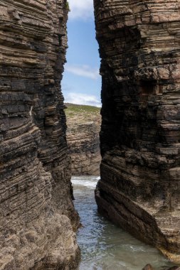 Aşağıdaki okyanus suyuyla dar bir geçit oluşturan dramatik kayalık kayalıklar engebeli kıyı jeolojisi ve mavi gökyüzünün bir anlık görüntüsünü sergiliyor.