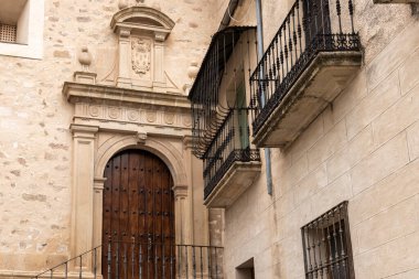 Çekici bir İspanyol kasabasında yıpranmış ahşap bir kapı, taş cephe ve demir balkon içeren antik mimari.