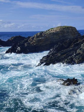 Okyanus dalgaları güneşli bir günde kayalık kıyı şeridine çarpıyor.