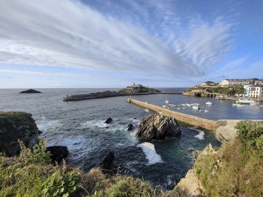 Tapia de casariego, Asterias, İspanya 'da liman, sakin sularda demirli tekneler, uzun bir iskele ve Kantabrian Denizi üzerinde dramatik bulutlar