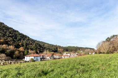 İspanyol kırsalındaki sarp tepelerin ve yemyeşil yeşilliklerin arasına yerleşmiş sakin bir köyün manzarası.