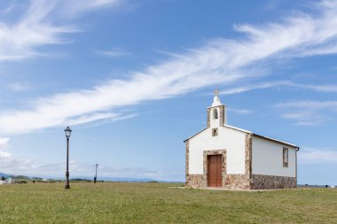 Güzel mavi gökyüzünün altında bulutlu yeşil bir çayırda duran küçük beyaz şapel.
