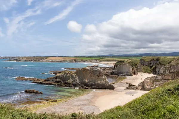 Dramatik uçurumlar, kumlu plajlar ve dinamik bir gökyüzü altında yuvarlanan yeşil tepeler içeren nefes kesici kıyı manzarası.