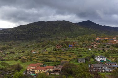 Tenerife, İspanya 'da bulutlu bir gökyüzünün altında yeşil tepeleri kaplayan küçük renkli evler ve çiftlikler.