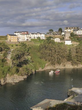 Büyüleyici bir galaksi köyünün sakin sularına demirlemiş iki balıkçı teknesi, yemyeşil ve geleneksel evlerle çevrili.