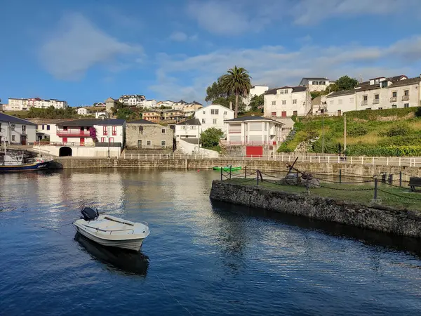 O Barqueiro 'nun limanının sakin sularında dinlenen küçük bir motorlu teknenin sakin manzarası. Geleneksel Galiçya evleri temiz mavi gökyüzünün altında rıhtımda asılıydı.