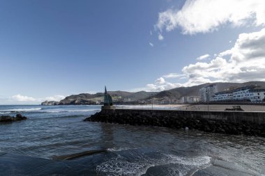 Güneşli bir günde İspanya, Ribadesella 'da deniz manzaralı, dağlı ve plajlı Asterian göçmenlerinin anıtı.