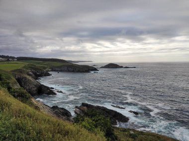 Bulutlu bir gökyüzünün altında engebeli uçurumlar ve dalgalar