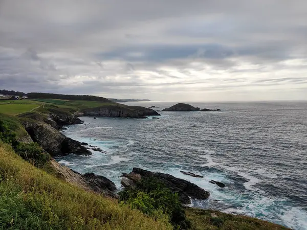 Bulutlu bir gökyüzünün altında engebeli uçurumlar ve dalgalar