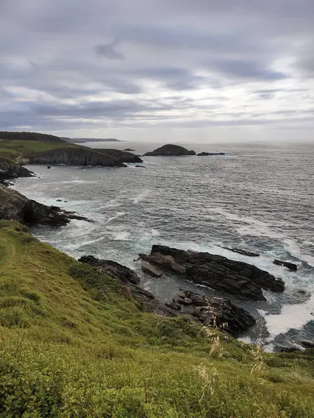 Okyanus dalgaları dramatik bulutlu bir gökyüzü altında kayalık bir sahile çarpıyor ve güzel bir deniz manzarası yaratıyor.