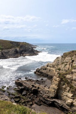 Güçlü okyanus dalgaları bulutlu bir gökyüzünün altında dramatik, kayalık bir kıyıya çarpar ve nefes kesici bir doğal manzara yaratır.
