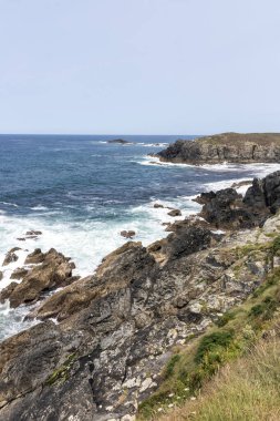 Güçlü okyanus dalgalarının bulutlu bir gökyüzünün altında engebeli, kayalık bir kıyı şeridine çarpması nefes kesici bir manzara.