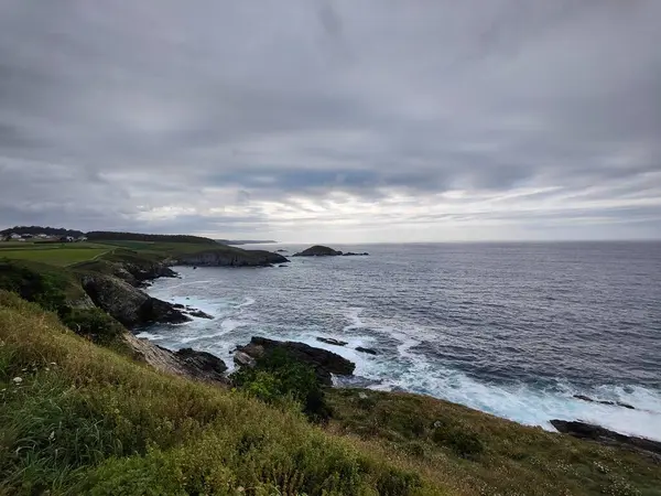 Dalgalar dramatik bulutlu bir gökyüzü altında kayalık bir sahile çarpıyor. Güzel ve güçlü bir deniz manzarası yaratıyor.