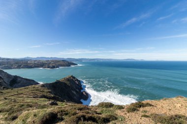 Kayalık bir kıyı şeridinin nefes kesen manzarası dingin mavi gökyüzünün altında engin okyanusla birleşerek pitoresk bir manzara yaratıyor.