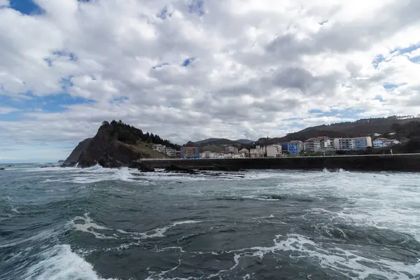 Okyanus dalgaları bulutlu bir gökyüzünün altında kıyı kasabası olan kayalık bir kıyı şeridine çarpıyor.