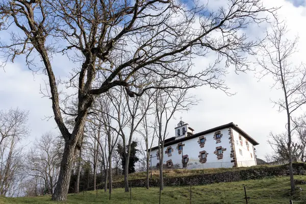 Kırsal kesimde bir grup çıplak ağacın arkasında çan kulesi olan beyaz bir inziva yeri.