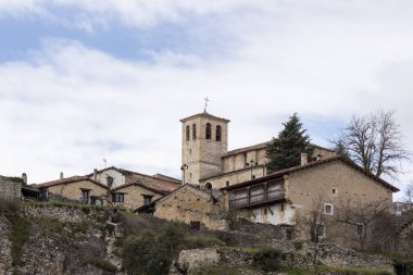 Tanınmış taştan bir kilise ve geleneksel evlerin yer aldığı tarihi bir İspanyol köyünün huzurlu manzarası, zamansız bir cazibe hissi uyandırıyor.