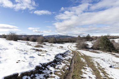 Kış manzarası, parlak mavi gökyüzünün altındaki uzak dağlara uzanan karlı bir yola ev sahipliği yapıyor.