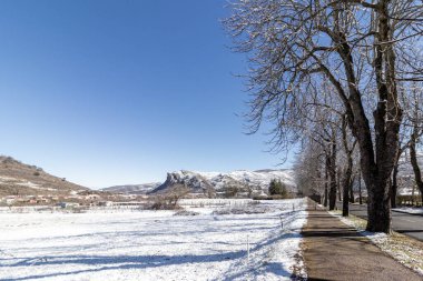 Kar, ağaçlar ve açık gökyüzünün altındaki uzak tepelerin olduğu kış manzarası.