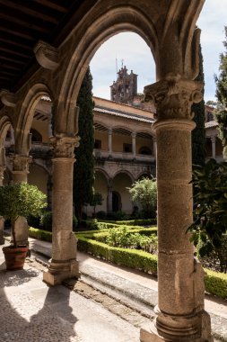 Güneş ışığı bir manastırın kemerlerinden süzülür, huzurlu bir bahçeyi aydınlatır ve taş sütunların süslü detaylarını aydınlatır.