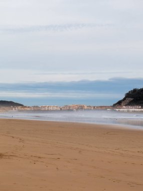 Laredo sahilinin bulutlu bir gökyüzünün altında okyanusla buluşup huzurlu bir kıyı manzarası yarattığı sakin bir manzara.