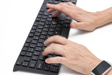 Eller beyaz bir masada, siyah bir klavyeye basıyor, akıllı bir kaset takıyor.