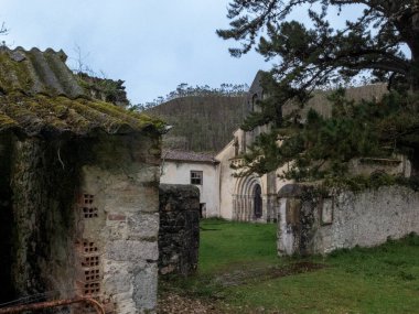 Eski taş binalar ve tarihi bir manastır yapısı yeşil çimen ve ağaçların arasında terk edilmiş duruyor.