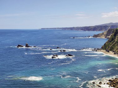 Okyanus dalgaları engebeli kayalıklarda kırılıyor ve kıyı şeridi boyunca tenha bir sahil var.