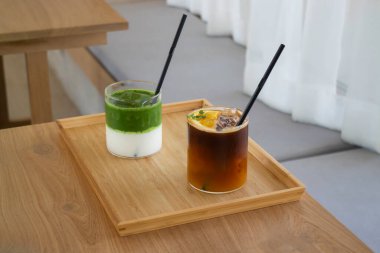 Buzlu kibrit çayı ve portakallı buzlu kahve, ahşap masanın üstünde.